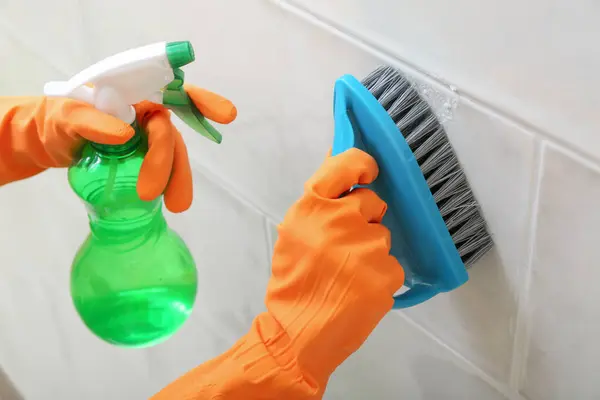 Woman in rubber gloves cleaning light tile with brush, baking soda and sprayer, closeup