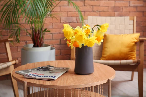 Vase with narcissus flowers and magazines on coffee table in living room