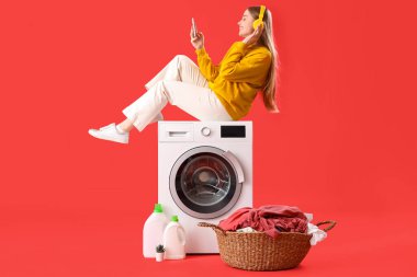 Güzel, genç bir kadın çamaşır makinesinde oturmuş kırmızı arka planda müzik dinliyor.