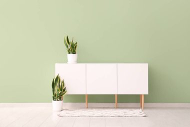 Çağdaş çekmeceler, yeşil duvarın yanında bitkiler.
