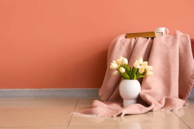 Ekoseli kitap, fincan ve pembe duvarın yanındaki vazoda laleler.