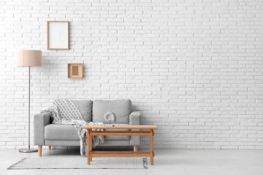 Beyaz tuğla duvarın yanında kanepesi ve lambası olan açık ahşap bir sehpa.