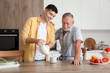 Genç adam mutfakta babası için sıcak çay dolduruyor.