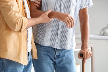 Genç adam babasına sopayla yardım ediyor. Mutfakta yürüyor, yakın plan.