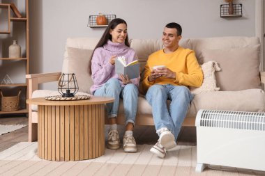 Evde kaloriferin yanında kitap ve çay ısıtan genç bir çift.