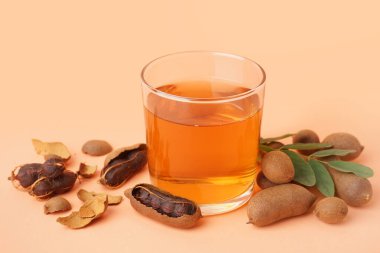 Bir bardak lezzetli demirhindi suyu ve turuncu arka planda meyveler.