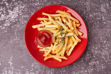 Gri arka planda ketçaplı lezzetli patates kızartması tabağı.