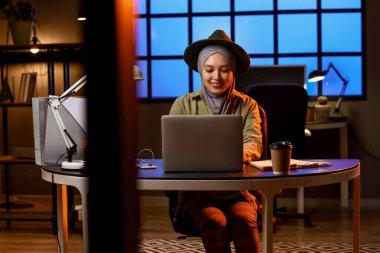 Genç Müslüman iş kadını geceleri dizüstü bilgisayarla ofiste çalışıyor.