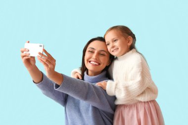 Genç anne ve küçük kızı mavi arka planda selfie çekiyorlar.