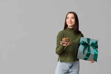 Gri arka planda hediye kutusu ve lezzetli kurabiyelerle güzel bir genç kadın.