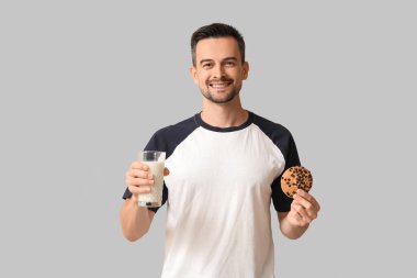 Lezzetli kurabiyesi ve gri arka planda bir bardak sütü olan yakışıklı bir adam.