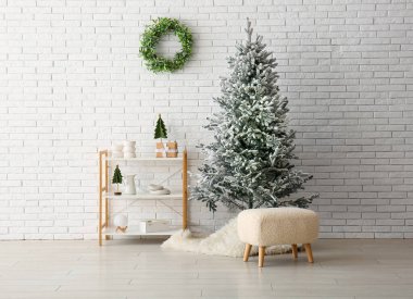 Beyaz tuğla duvarın yanında rafları ve minderleri olan güzel bir Noel ağacı