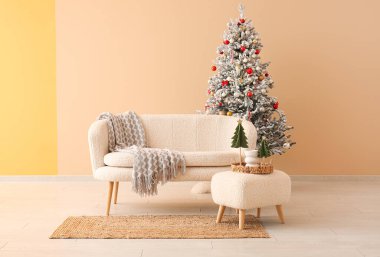 Güzel Noel ağacı ve bej duvarın yanında rahat bir kanepe.