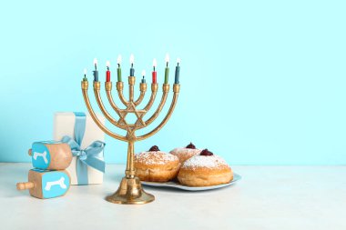 Menorah, tasty donuts and dreidels for Hanukkah celebration on table against color background clipart