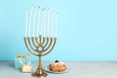 Yanan mumlar, donut ve Hanuka kutlaması için hediyeli menorah renk arka planına karşı masada.