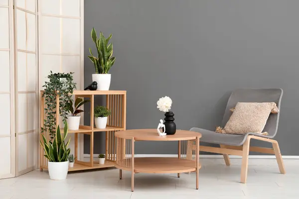 Light wooden coffee table with shelving unit and armchair near grey wall