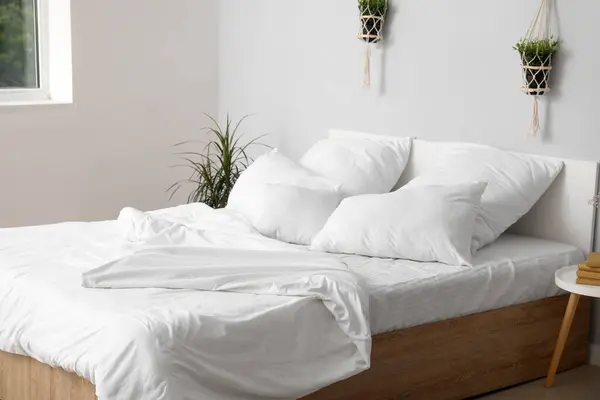 Large double bed with white pillows and houseplants in interior of light bedroom