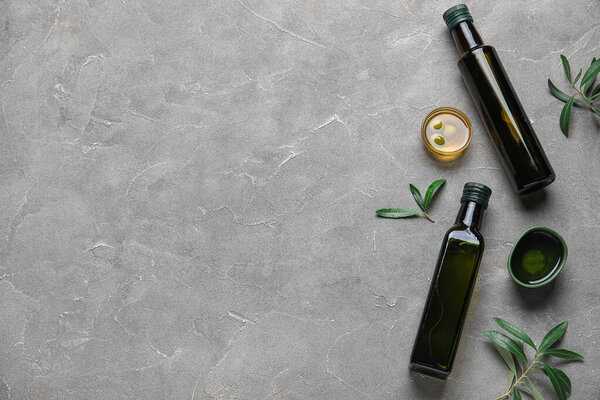 Бутылки и миски свежего оливкового масла на сером фоне