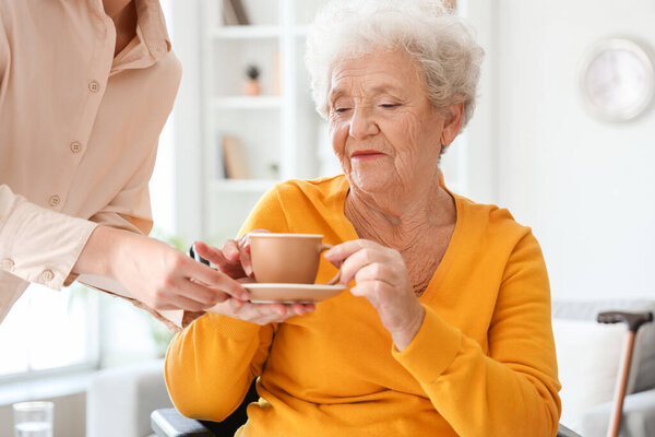 Senior woman taking cup of tea from her daughter at home