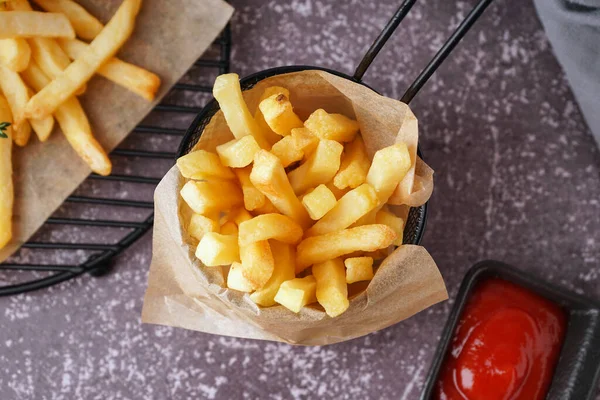 Deep fryer basket with french fries and ketchup on grey background