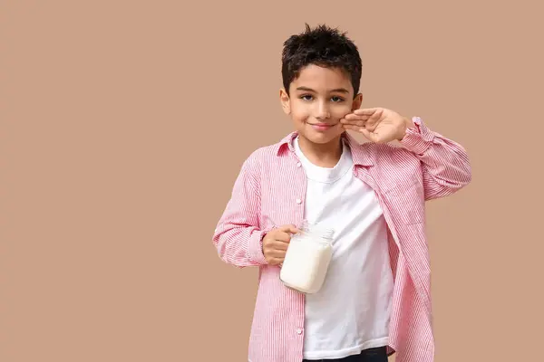 Cute little boy with mason jar of milk on beige background