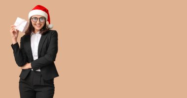 Noel Baba şapkalı güzel bir iş kadını ve bej arkaplanlı bir Noel hediyesi ve mesaj için yeri var.