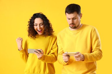 Sarı arka planda cep telefonu kullanan genç bir çift.