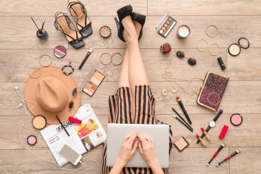 Dizüstü bilgisayarı ve aksesuarları olan bir kadın açık tahta zeminde oturuyor.