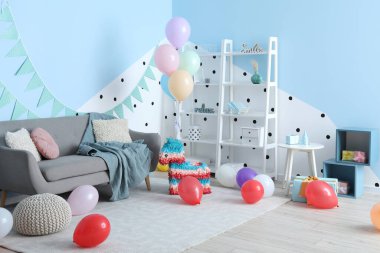 Doğum günü için dekore edilmiş oturma odasının içinde balonlar, pinyatalar ve çelenkler var.