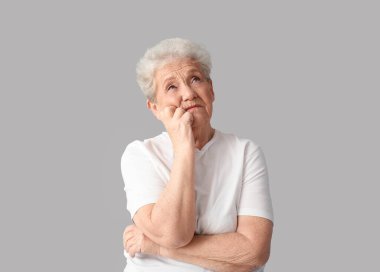 Gri arka planda düşünceli yaşlı bir kadın.