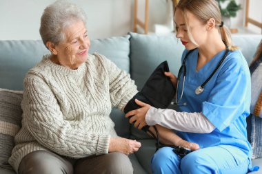 Evde yaşlı bir kadının tansiyonunu ölçen genç bir bakıcı.