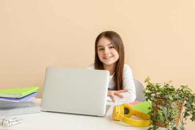 Dizüstü bilgisayarı olan küçük bir kız bej arka plan hakkında ders veriyor.