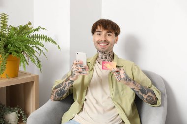 Evde cep telefonu kullanan dövmeli genç bir adam.