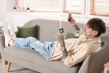 Evde cep telefonu kullanan dövmeli genç bir adam.