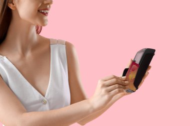 Pembe arka planda kredi kartıyla ödeme yapan genç kadın, yakın plan.