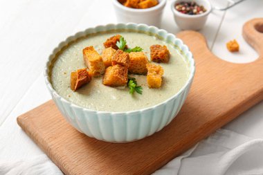 Beyaz ahşap zemin üzerinde kızarmış ekmeklerle bir kase lezzetli krema çorbası.