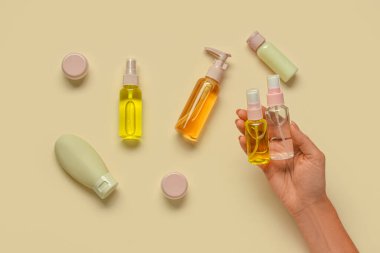 Renk arkaplanında seyahat kozmetik seti olan bir kadın eli