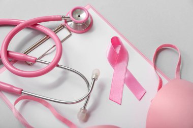 Pink ribbon with stethoscope, bra and clipboard on grey background. Breast cancer awareness concept clipart