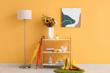 Sonbahar çiçekleri, balkabakları ve turuncu duvarın yanında dekor olan raf ünitesi.