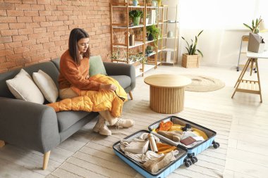 Evde kışlık giysileri bavula koyan genç bir kadın.