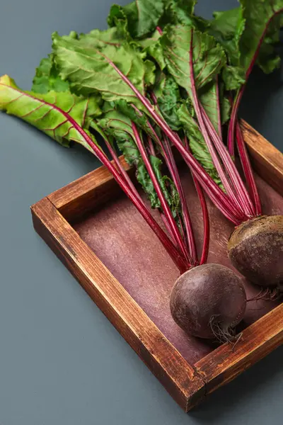 Fresh beetroot with leaves in wooden plate on grey background