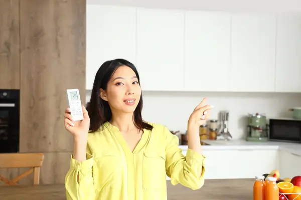 stock image Beautiful Asian woman switching on air conditioner in kitchen