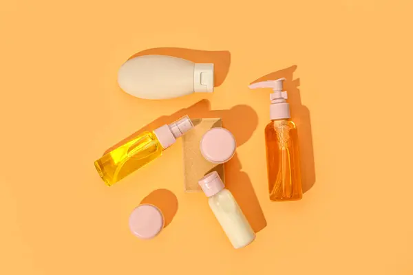 Stand with set of travel cosmetic products on orange background