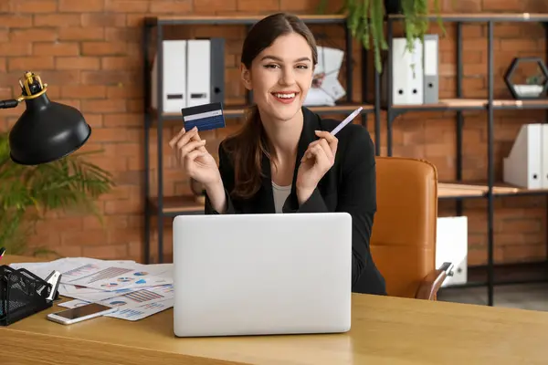 Young businesswoman with credit card at table in office