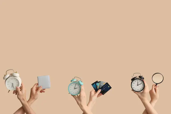 Hands holding alarm clocks, credit cards and magnifier on beige background