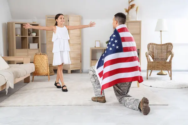 Little girl running to her military father with USA flag at home. Veterans Day celebration