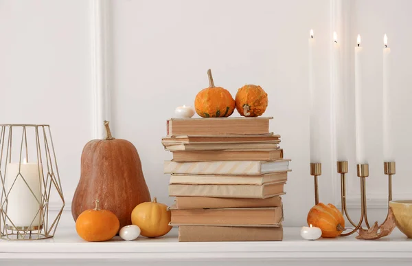 Pumpkins, books and burning candles on mantelpiece in living room, closeup