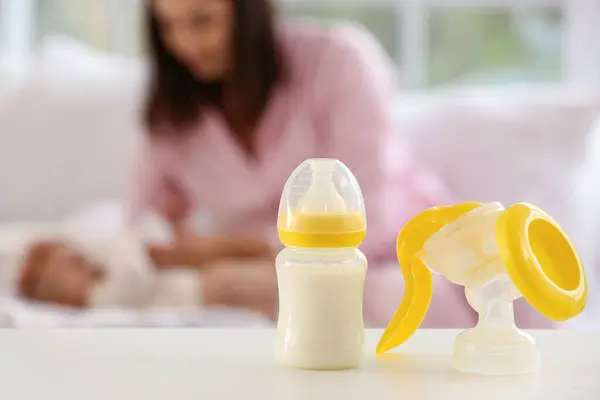 Breast pump with baby bottle of milk on table in bedroom, closeup