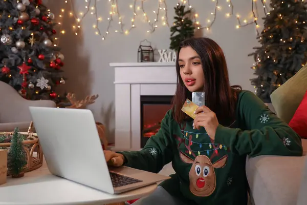 Young woman with credit cards and laptop shopping online for Christmas at home