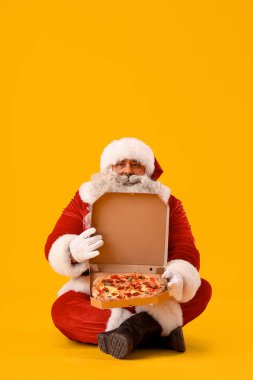 Sarı arka planda oturan lezzetli pizzalı Noel Baba